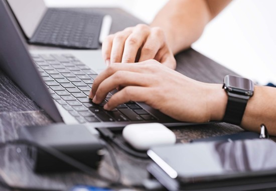 ノートパソコンのキーボードを叩く男性の手を写した写真